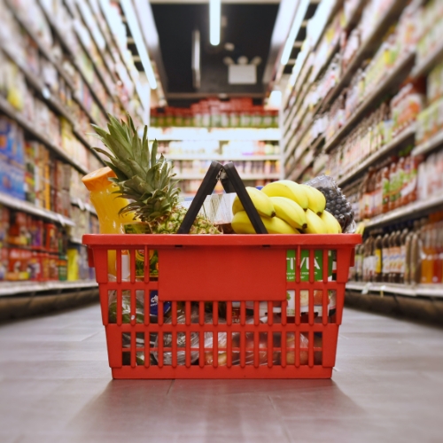 Czerwony koszyk pełen zakupów spożywczych w alei supermarketu